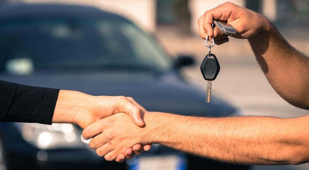Hands are shaking and a car key is being handed over in front of a used car.