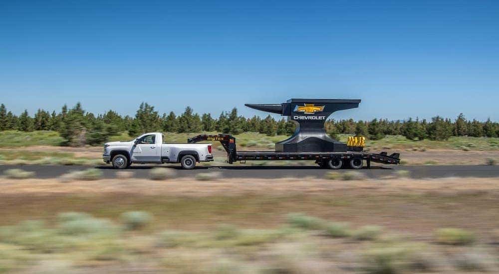 A white 2020 Chevy Silverado 3500HD is shown from the side towing a large anvil with a Chevrolet logo.