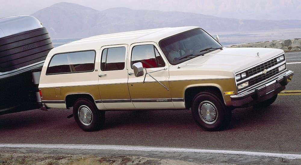 A tan two-tone 1991 used Chevy Suburban is towing a camper on a mountain road.