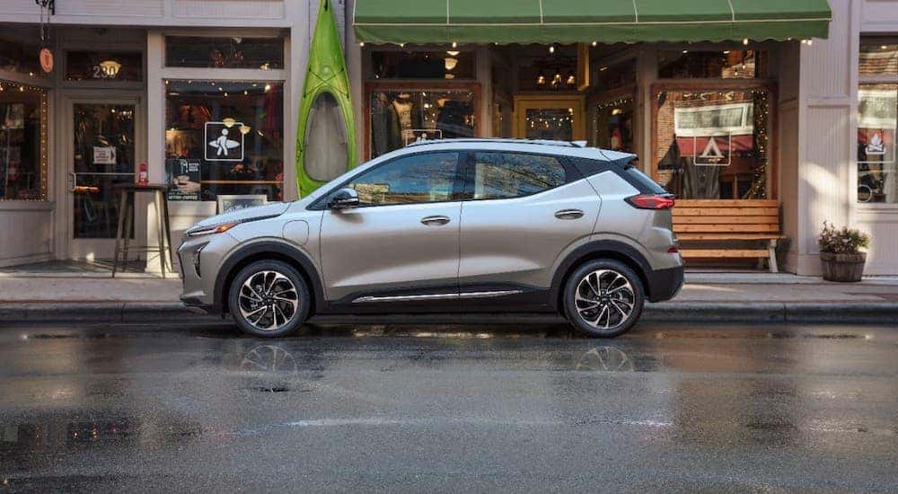 A new Chevy EV, a silver 2022 Chevy Bolt EUV, is parked on a street in front of shops.