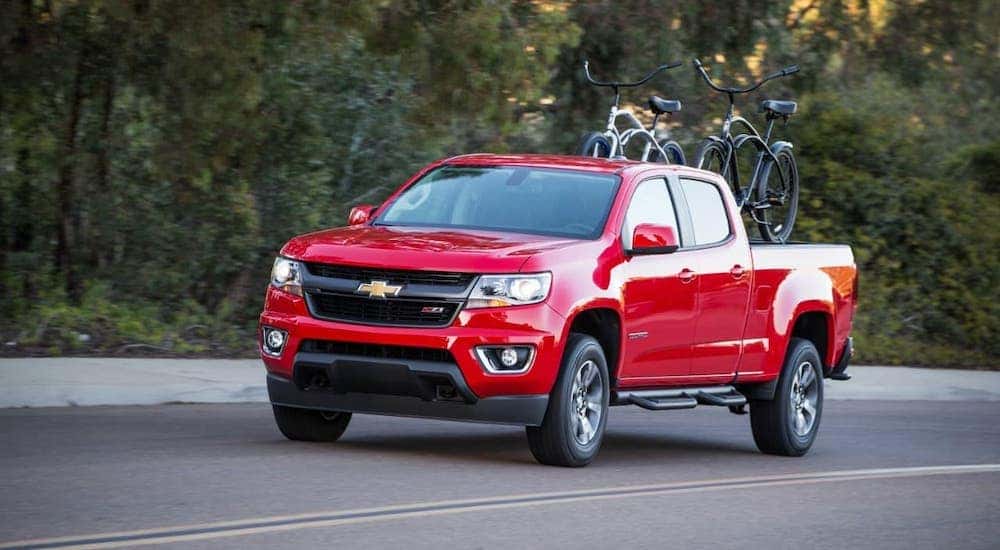 A red 2017 Chevy Colorado is driving on a tree-lined road with bikes in the bed.