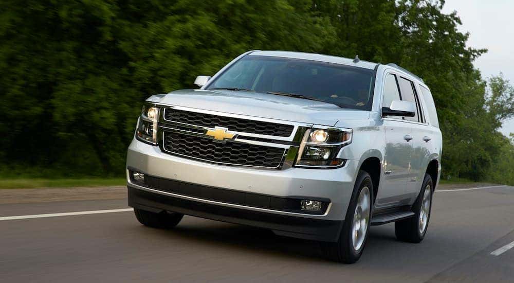 A silver 2015 used Chevy Tahoe LT is driving down a tree lined road.