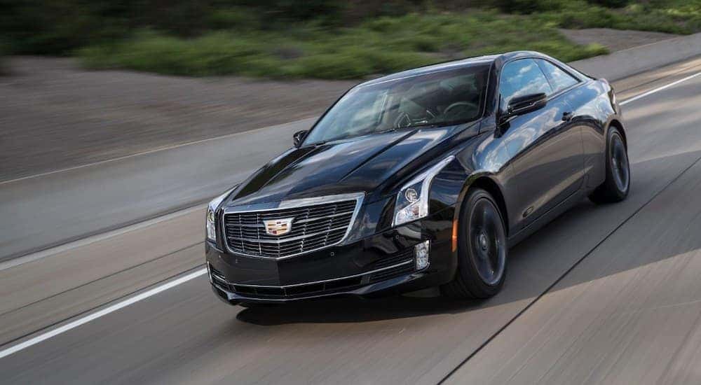 A black 2018 Cadillac ATS Coupe is driving fast on a rural road.