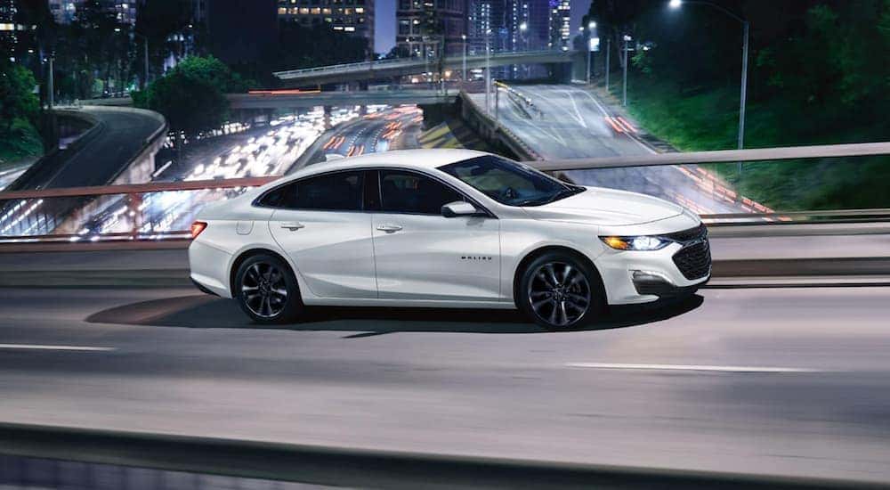 A white 2021 Chevy Malibu is shown driving on a bridge after visiting a used Chevy dealership near Carlisle.
