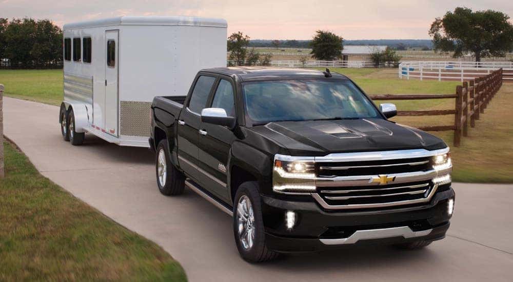 A black 2018 Chevy Silverado 1500 High Country is shown towing a white trailer.