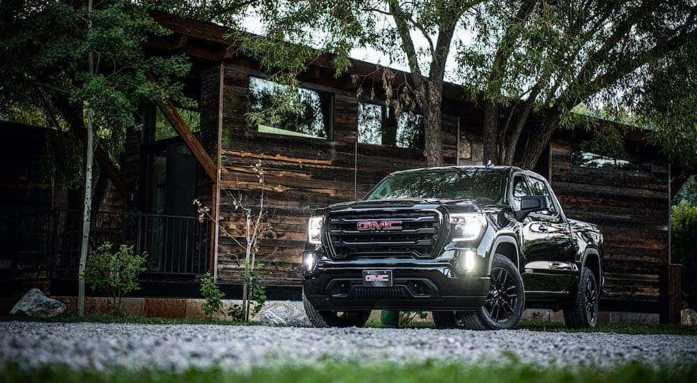 A newer used diesel truck, a black 2020 GMC Sierra SLE Elevation, is parked in front of a cabin in the woods.