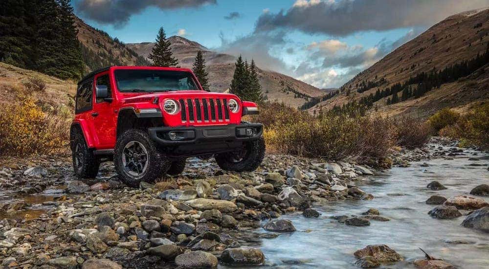 A red 2019 used Jeep Wrangler is parked in front of a mountain river.