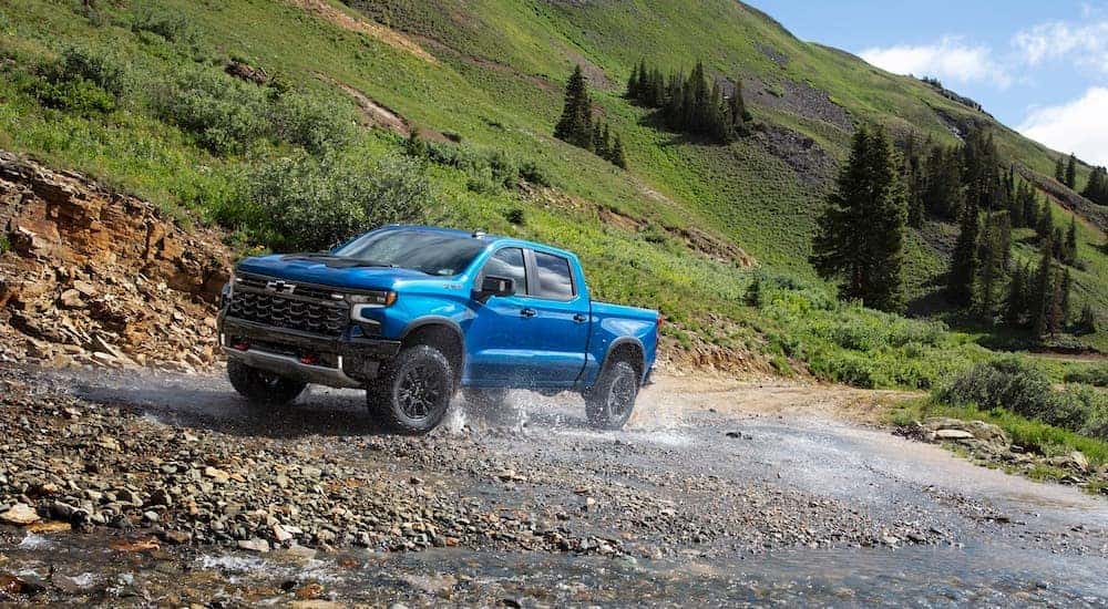 A blue 2024 Chevy Silverado 1500 ZR2 is shown from the front at an angle while driving through shallow water.