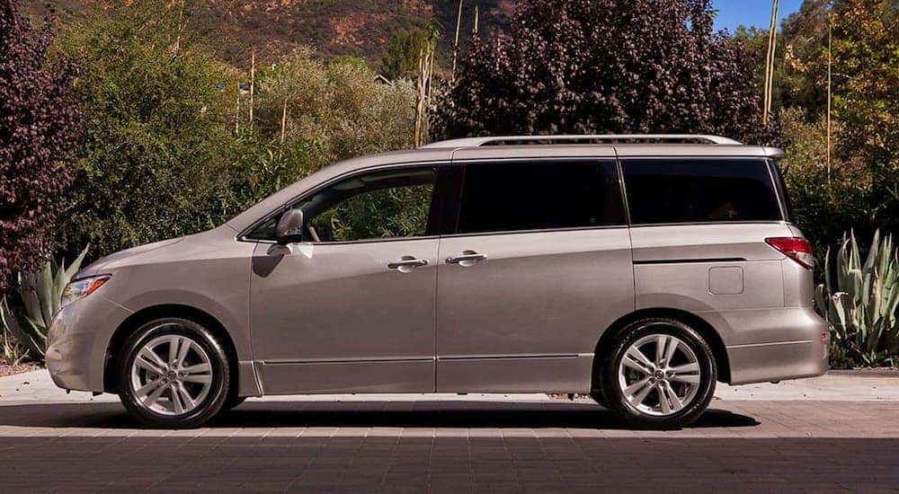 A silver 2016 Nissan Quest is shown from the side while parked in front of a plants.