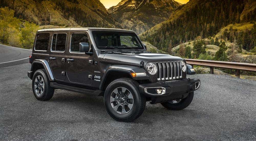 A gray 2019 used Jeep Wrangler Unlimited is parked in front of mountains and a yellow sky.