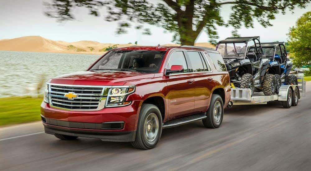 A red 2015 used Chevy Tahoe LS is towing a trailer with two UTVs.