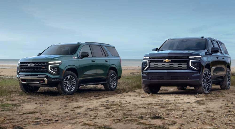A teal 2025 Chevy Tahoe Z71 parked next to a black 2025 Chevy Suburban High Country on the beach.