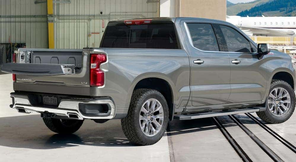 A grey 2021 Chevy Silverado 1500 from a Chevy dealership near me has the upper portion of the multi function tailgate open while at an airport.