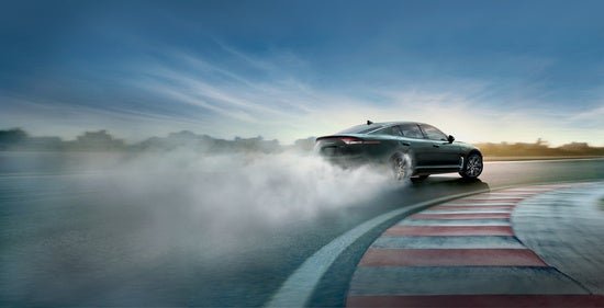 2023 Kia K5 drifts dramatically around a wet racetrack, leaving a trail of smoke.