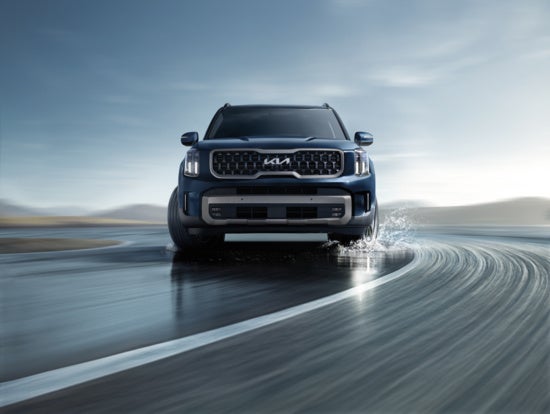 2025 Kia Telluride with a prominent grille and sleek design is driving swiftly around a wet, curving track.