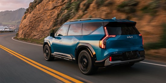 Kia EV9 with sleek design features drives along a winding coastal road.