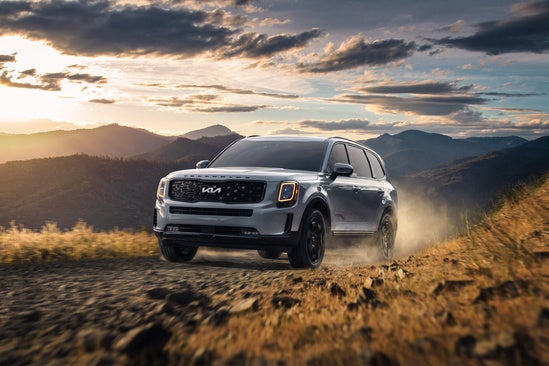 Kia Telluride driving along a rugged dirt road in a mountainous landscape.