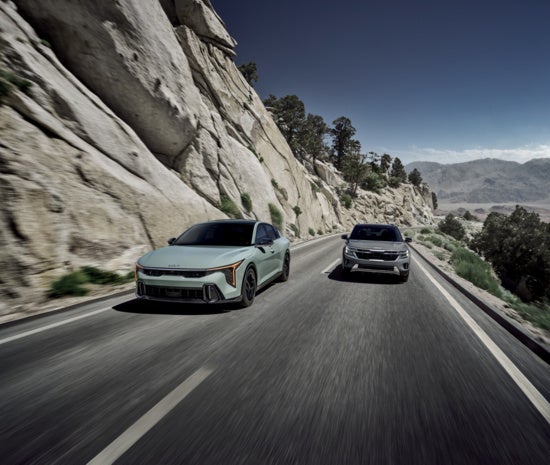 Two Kia cars navigating a scenic mountain road.