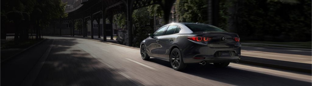 Mazda 3 driving along a bustling city street, surrounded by modern buildings and urban scenery.