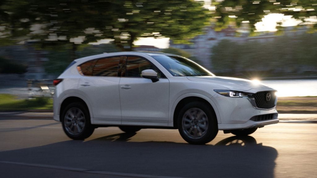 A Mazda CX-5 drives along a bustling city street, surrounded by tall buildings and urban scenery.
