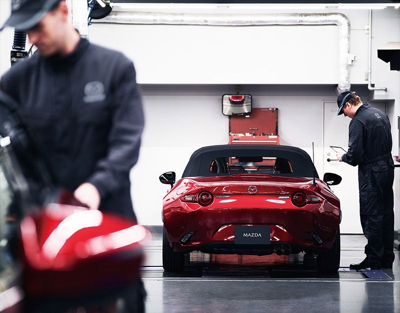 A man is engaged in repairing a red sports car in a factory setting, showcasing his expertise and concentration.