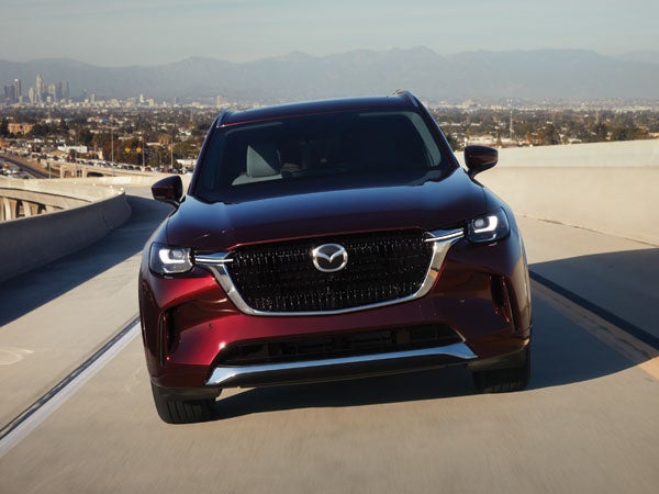A Mazda CX-90 driving along a highway under a clear blue sky.
