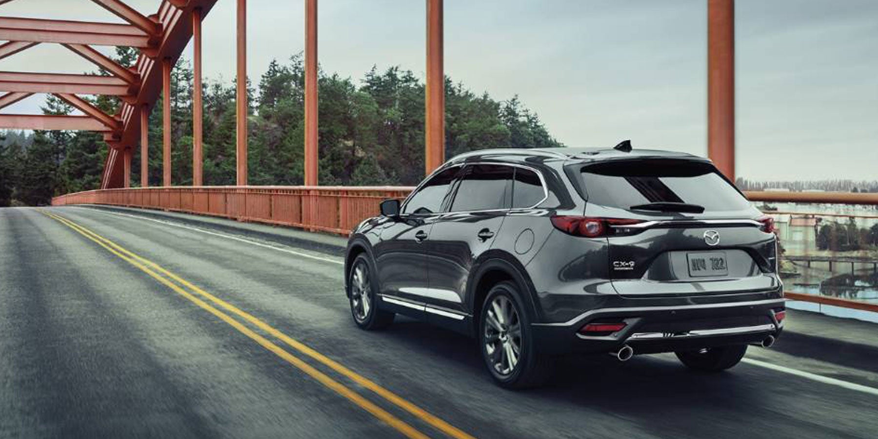 A Mazda CX-9 driving across a bridge with a scenic view in the background.