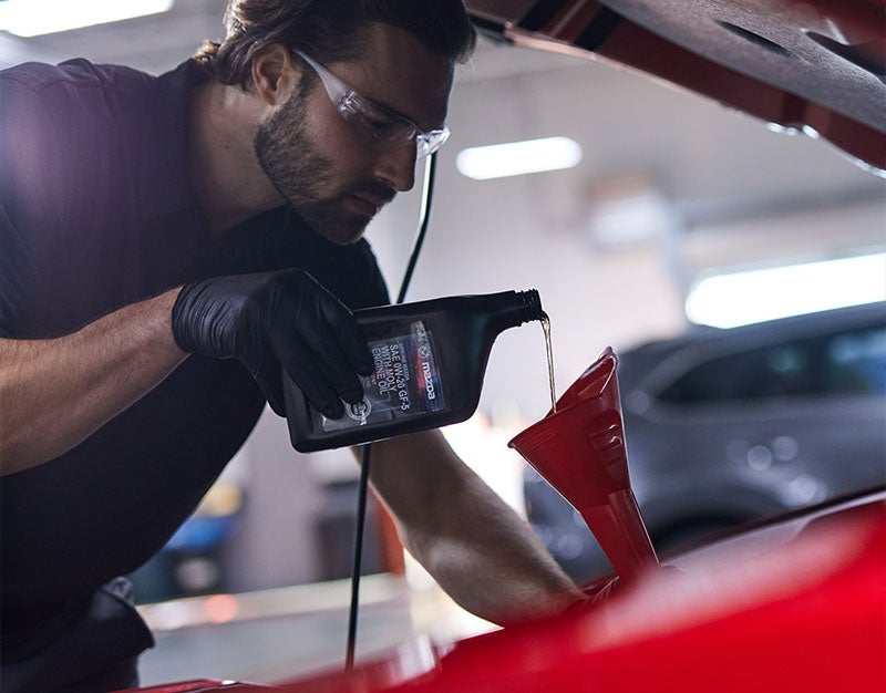 A man is adding oil to a car engine, demonstrating routine vehicle upkeep and care.