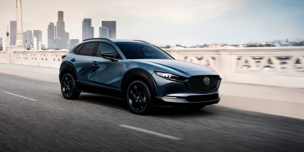 A Mazda CX-30 driving along a bustling city street, showcasing its sleek design and urban environment.