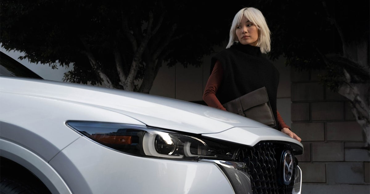 Woman standing beside a white Mazda CX-5 SUV front view at dusk