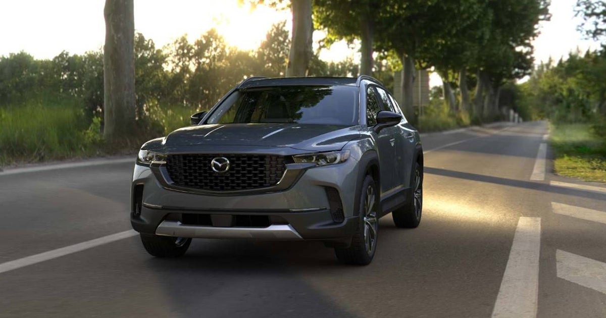 Mazda CX-50 front view driving on road with trees at sunset