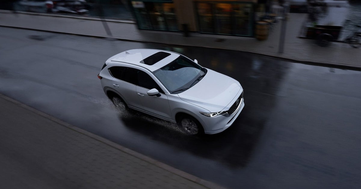 White SUV driving on a wet city street, seen from above.