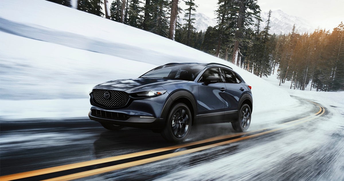 Mazda CX-30 SUV driving on snow-covered mountain road with trees