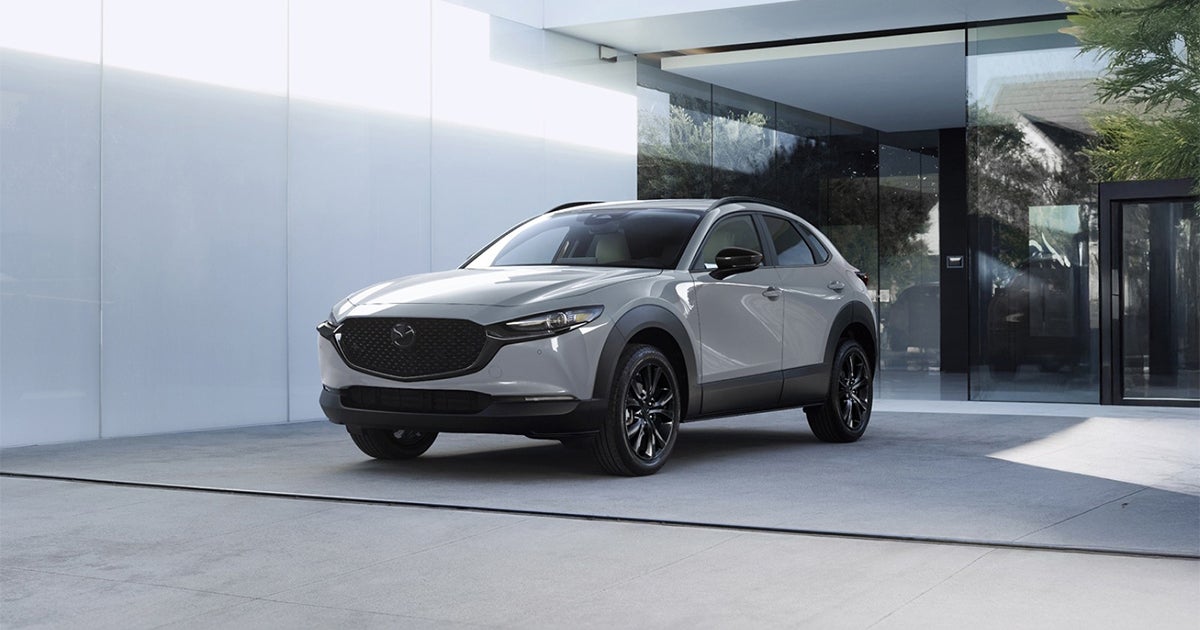 Gray Mazda CX-30 SUV parked outside modern glass home