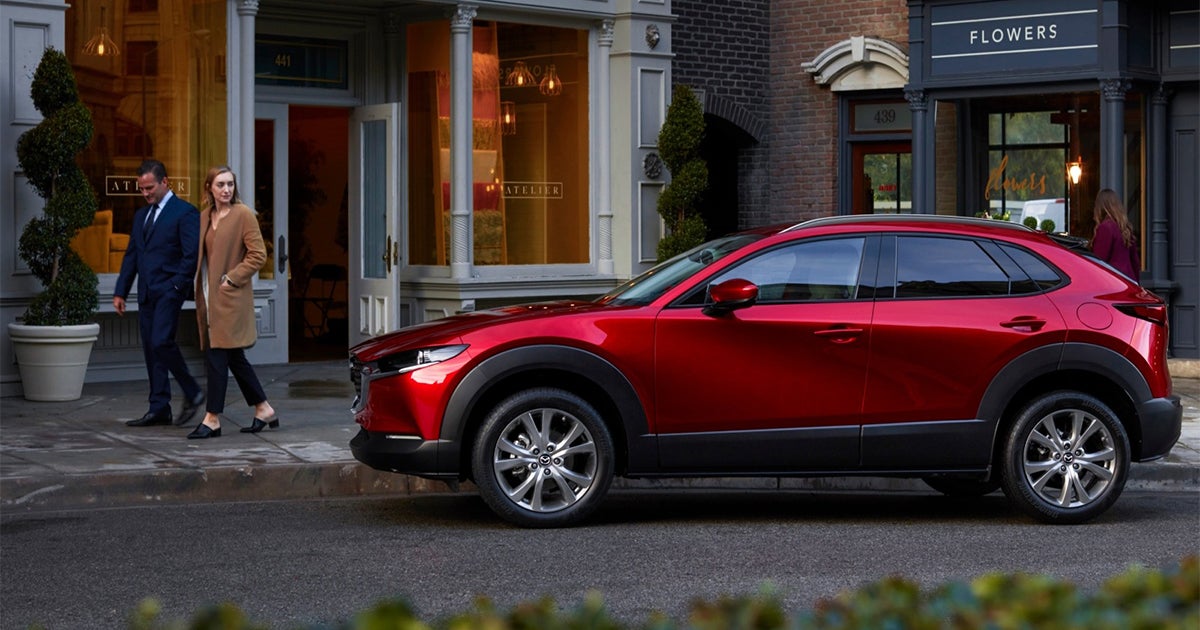 Red Mazda CX-30 parked on city street with couple walking nearby