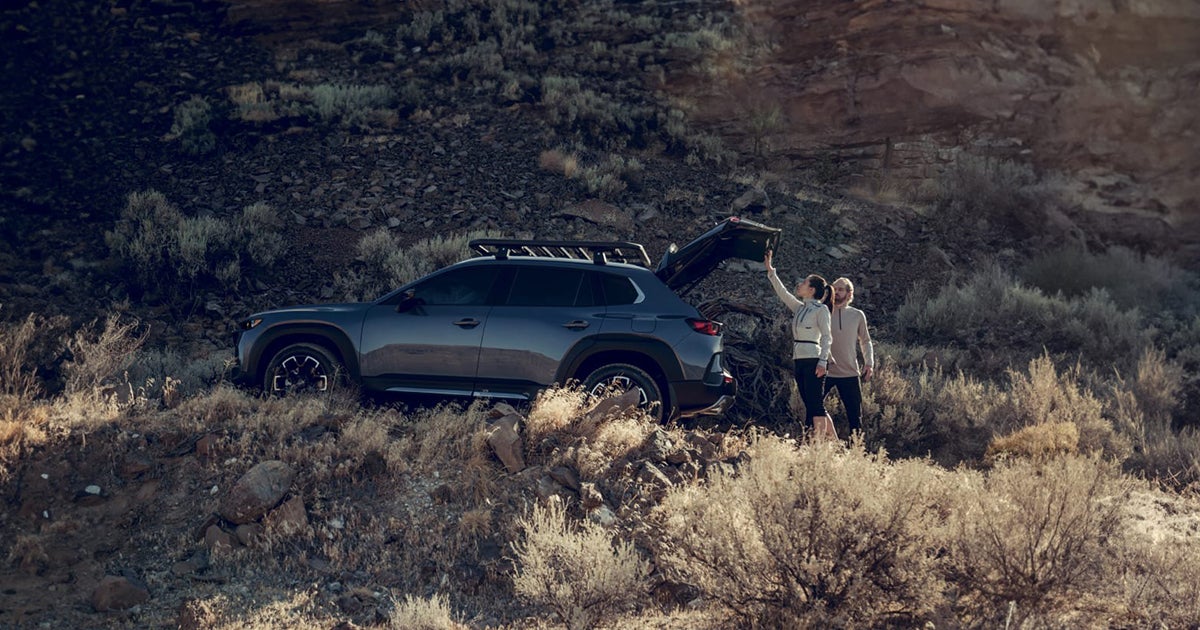 Mazda CX-50 SUV parked on rocky hillside with couple loading gear