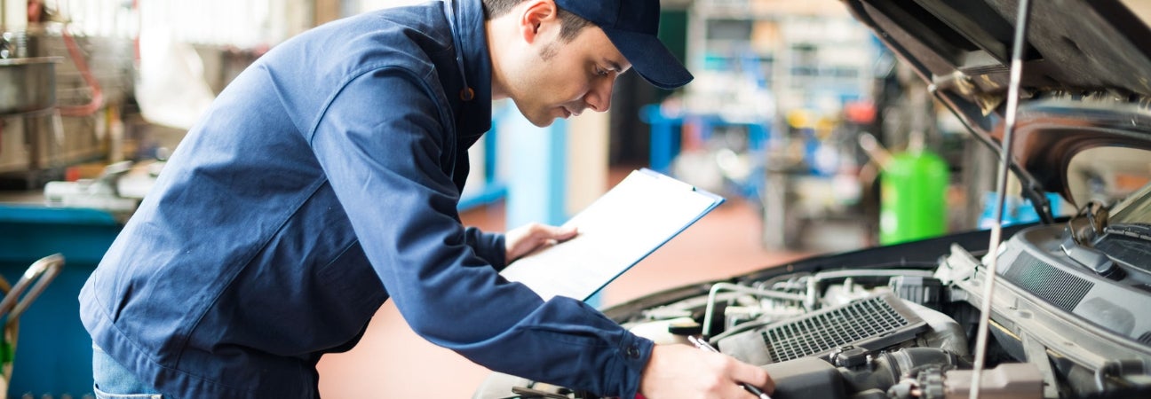 Car technician under the hood of a car with a clipboard.