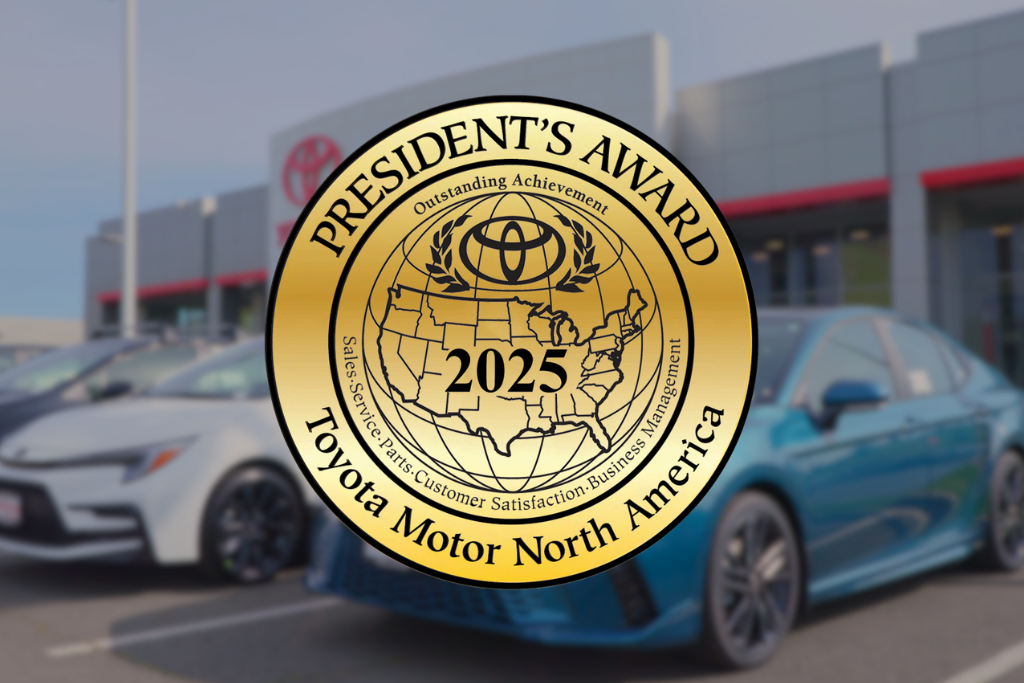 Gold “President’s Award 2025” seal from Toyota Motor North America over a blurred car dealership background with parked vehicles.