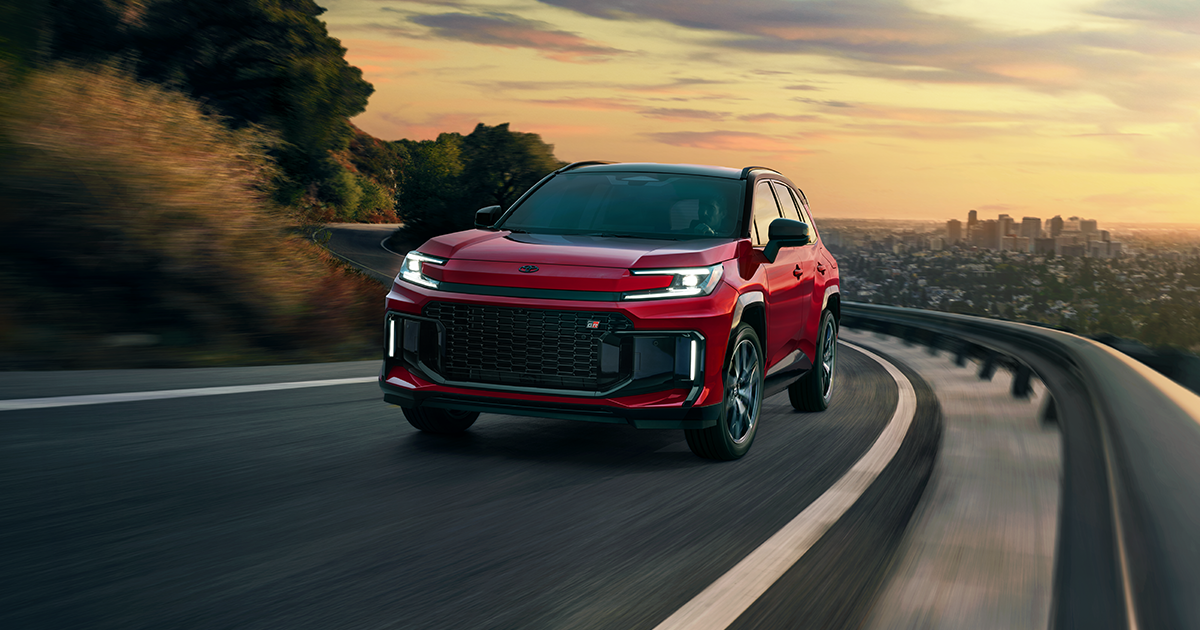 A red 2026 Toyota RAV4 GR Sport Plug-In Hybrid driving up a road during sunset