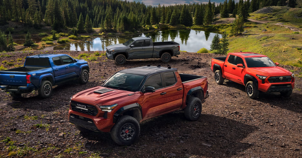 Four 2024 Toyota Tacoma models in various colors and trims parked in outside off road in a park.