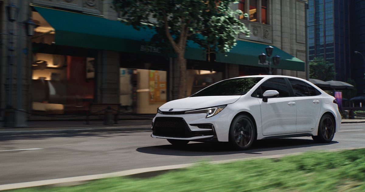 A white Toyota Corolla driving through city streets.