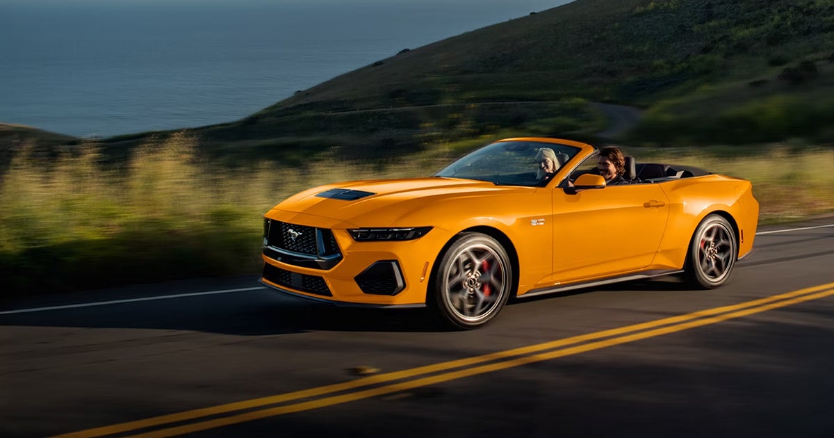 A yellow Ford Mustang convertible with the top down on the road.