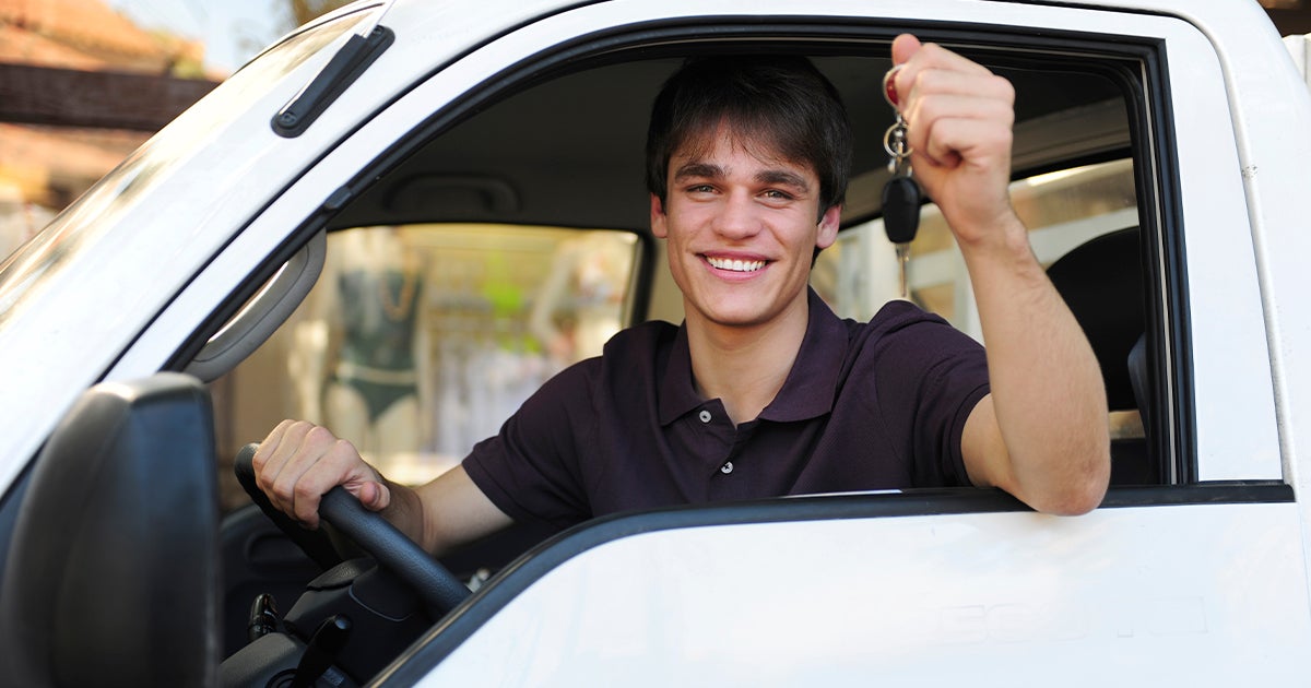 A happy driver holding up his car keys while sitting in the car.