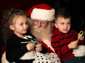 A boy and a girl sitting on Santa's lap with candy canes.
