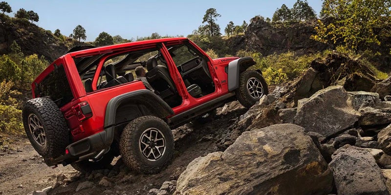 A red Jeep Wrangler climbing over rocks in an off-road environment