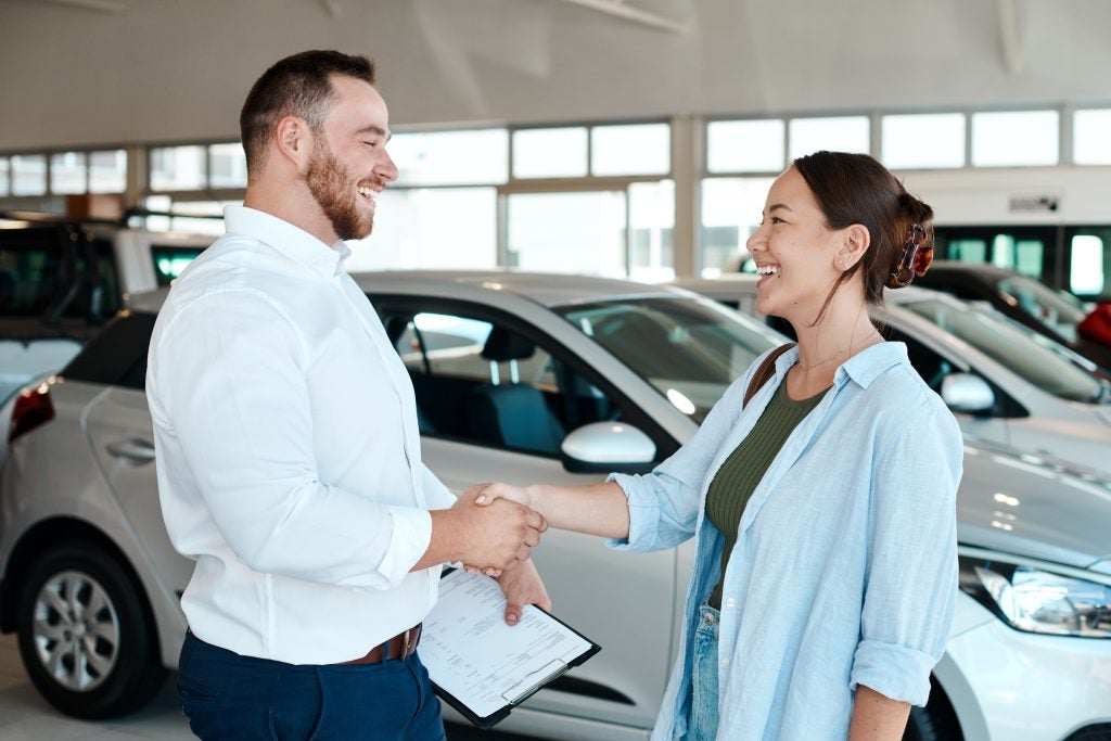Car dealership salesperson shaking hands with a customer during a vehicle purchase.
