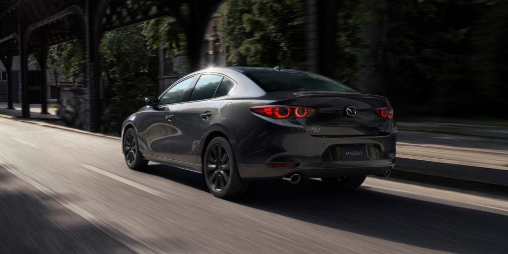 Alt text: A Mazda3 sedan driving on a city street with motion blur, showcasing its sleek design and rear view.