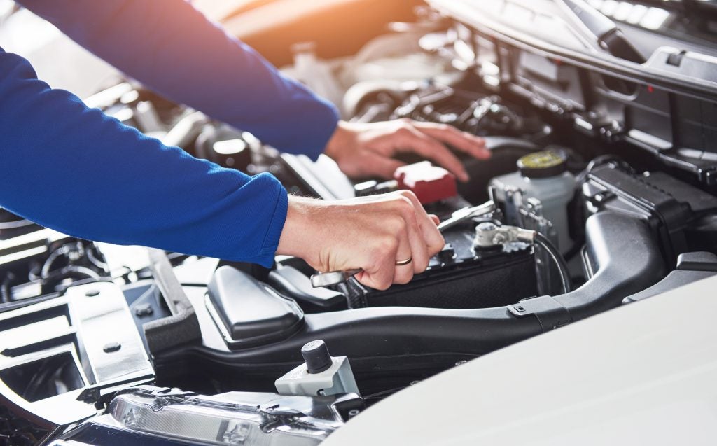 Mechanic working under the hood of a car engine during maintenance.