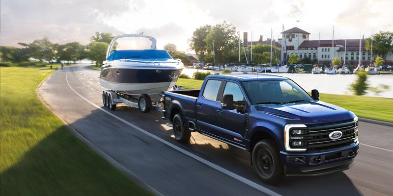 Blue pickup truck towing a boat along a lakeside road