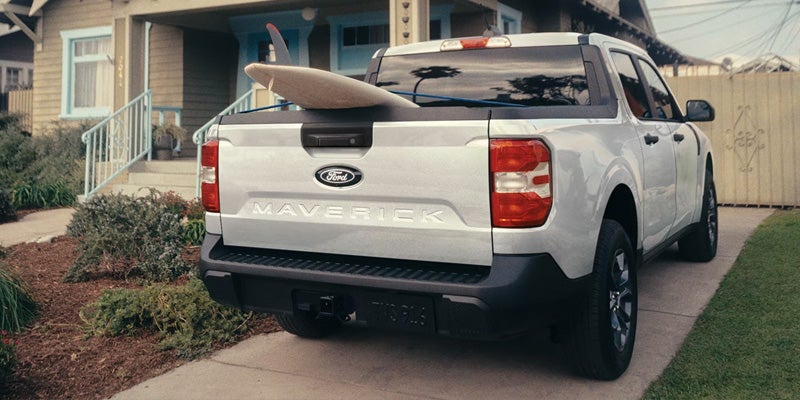 White Ford Maverick pickup with surfboard in bed parked in driveway